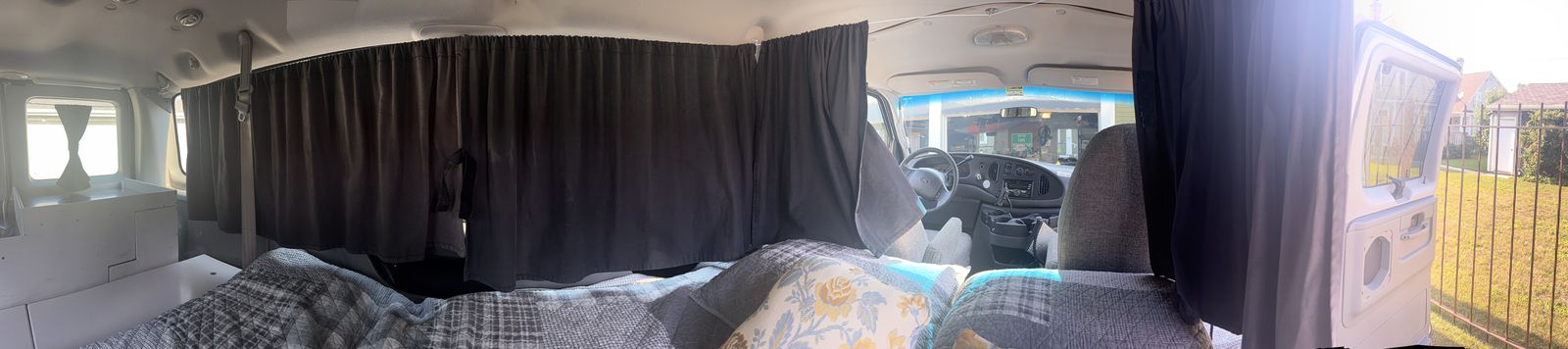 The inside of a Color Wagon camper end to end: rear kitchen, blackout privacy curtains, a made-up queen bed, the driver's cab and the open side door